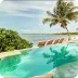 A stunning tropical beach with clear turquoise waters, palm trees, and a luxurious infinity pool overlooking the ocean, showcasing The Husna Experience.