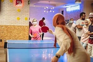 People playing table tennis at a social event, with spectators and a welcoming atmosphere.