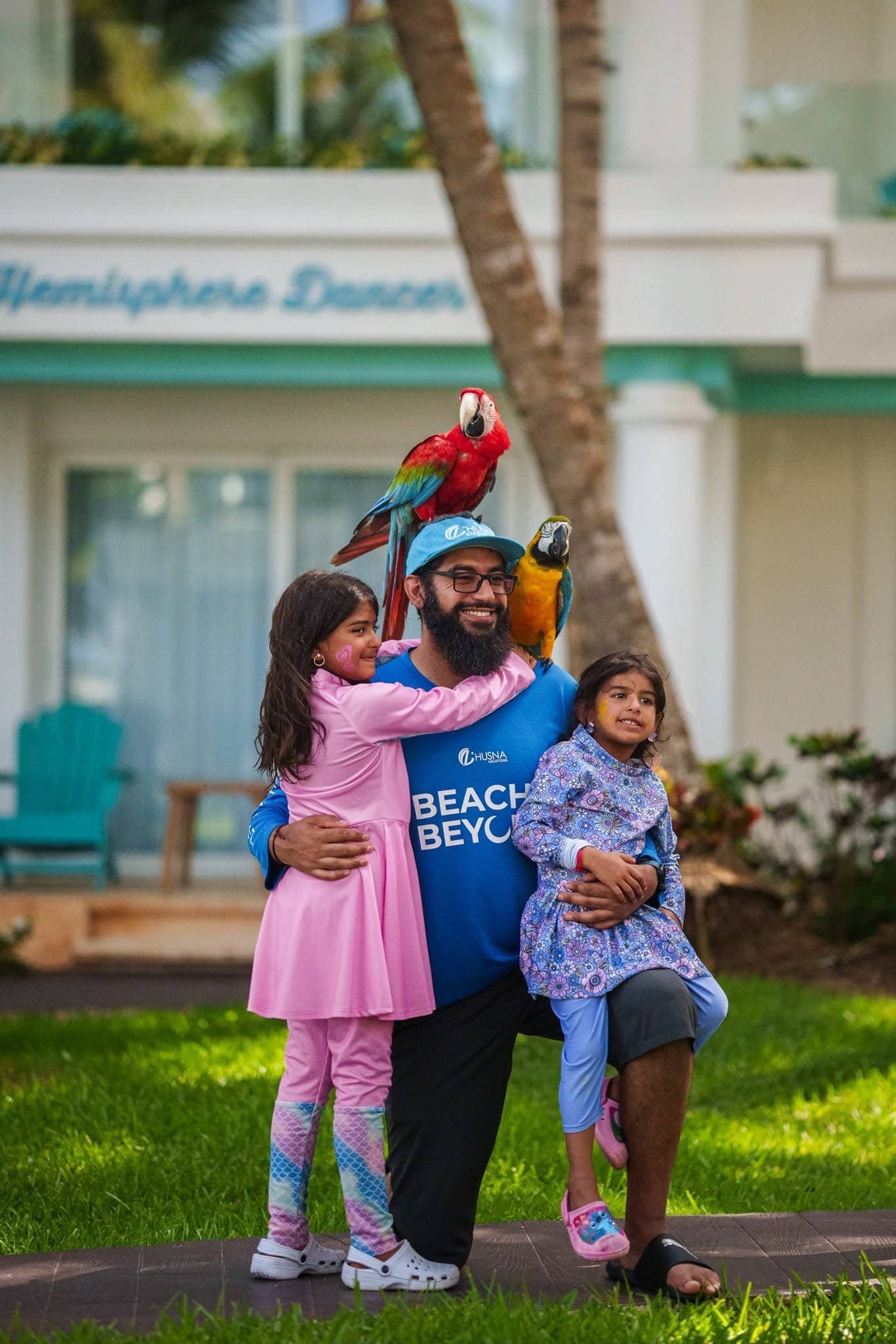 Happy family enjoying the Beach & Beyond Experience with colorful parrots in a tropical resort setting. Perfect for adventure and family travel enthusiasts.