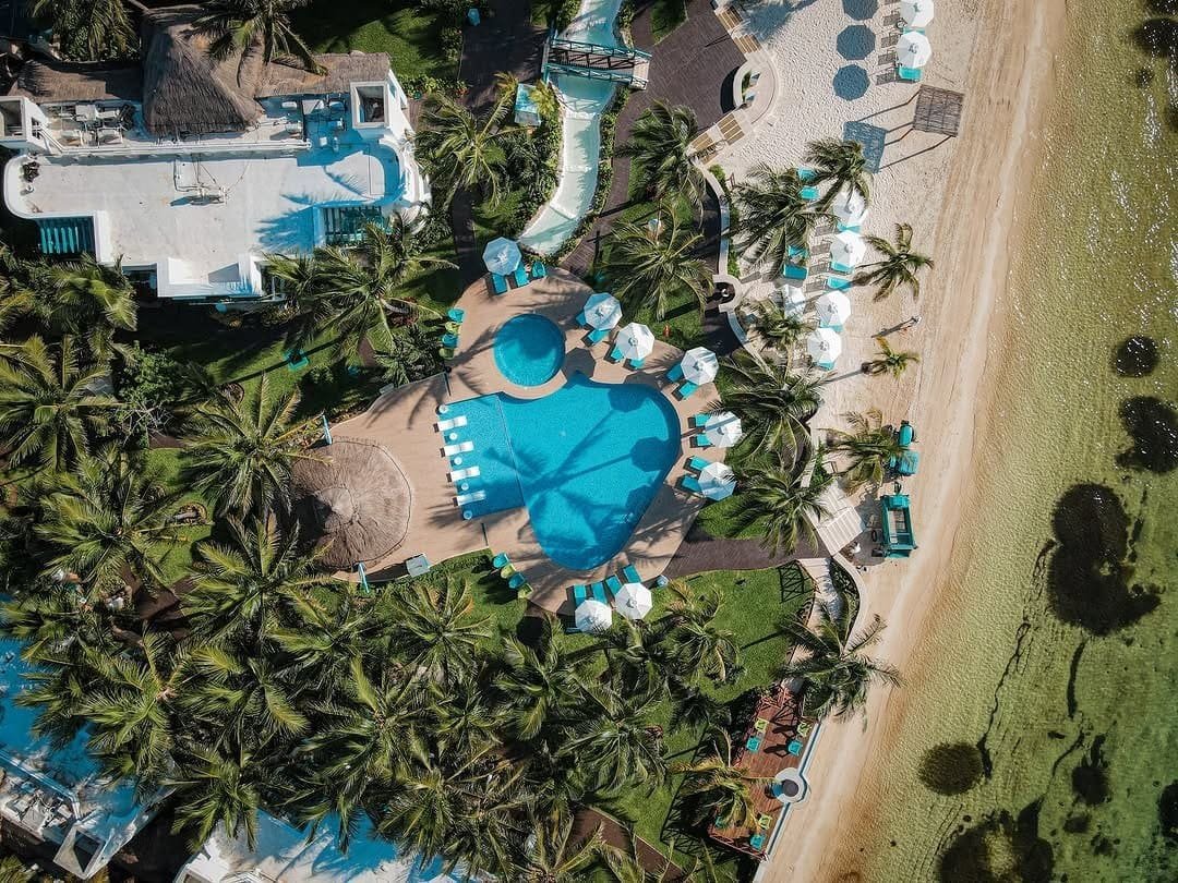 Aerial view of Husna Resort showcasing a large swimming pool surrounded by palm trees, sun loungers, and tropical landscaping, offering a luxurious and relaxing vacation experience.